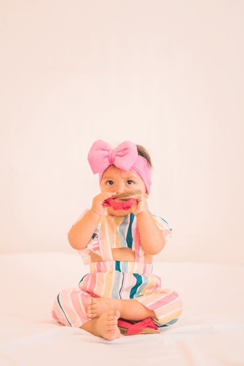 Free Girl in Striped Jumpsuit Wearing Pink Headband Putting Sandal on Her Mouth Stock Photo