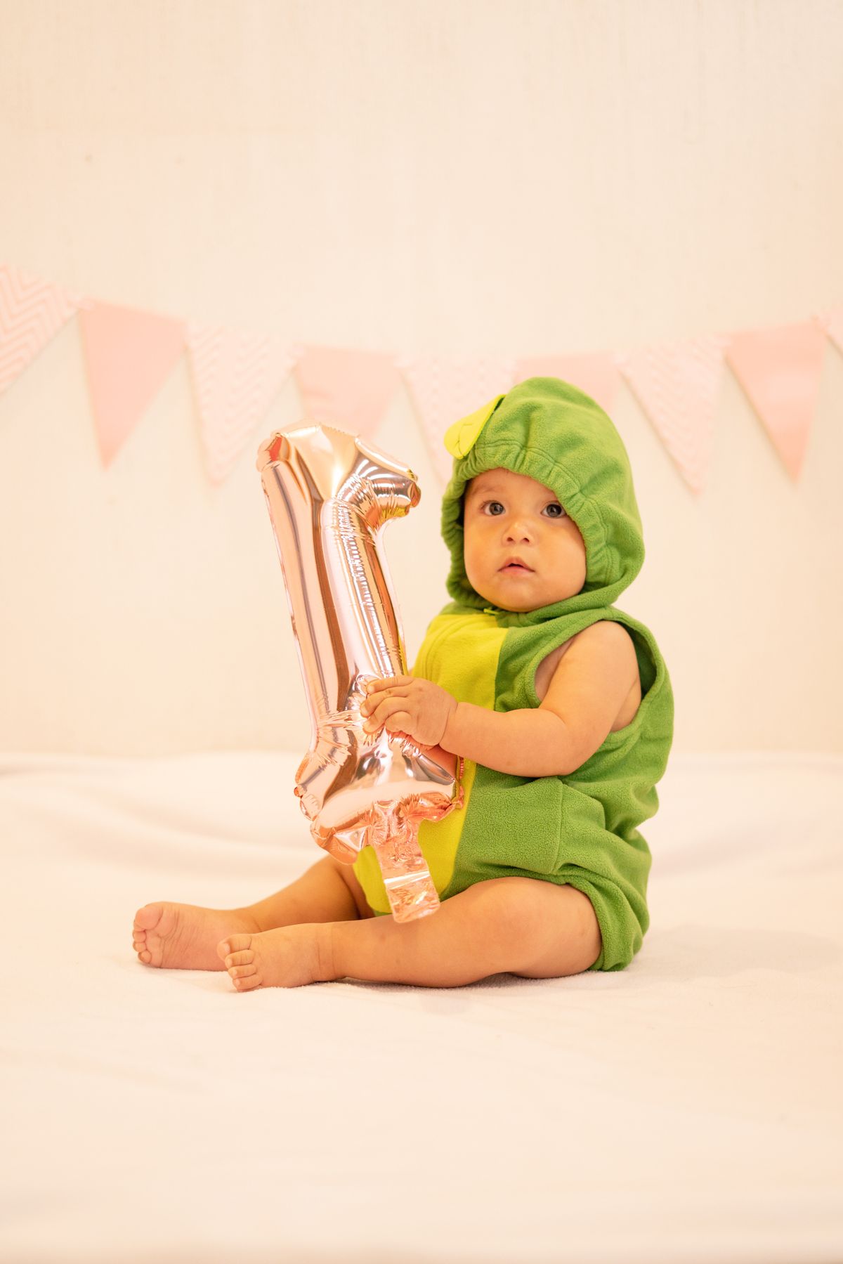 Cute baby in a dinosaur costume holding a number one balloon in a studio setting. Stock Photo.
