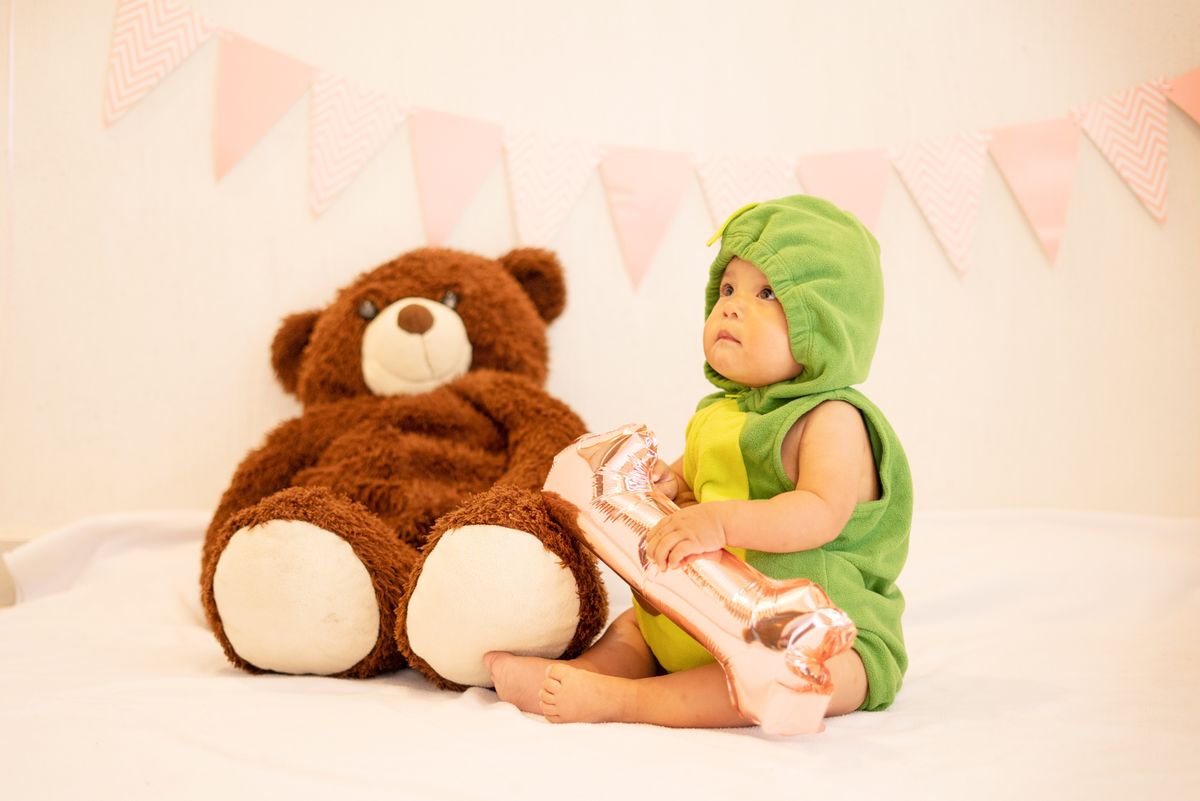 Cute baby in dinosaur costume sitting with a large teddy and playful decor. Stock Photo.