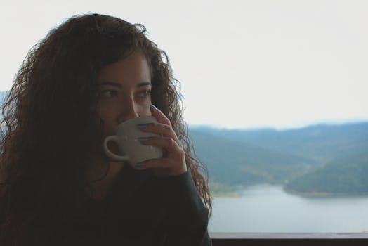 一位卷发女人在风景优美的山脉背景下，于室内喝着咖啡