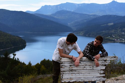 Two Person Standing at the Back of White Wooden Board Near the Body of Water