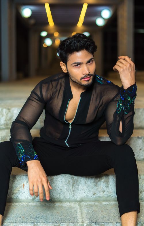 Free Confident male model in a fashionable black sheer top posing elegantly indoors. Stock Photo