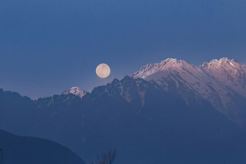 Free A captivating full moon rising over serene snow-capped mountains under a clear blue sky. Stock Photo