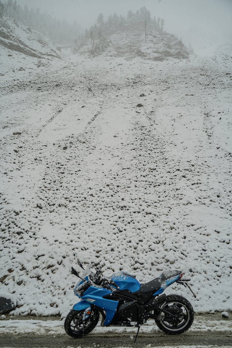 A Blue Motorcycle Parked Near The Snow Covered Mountain