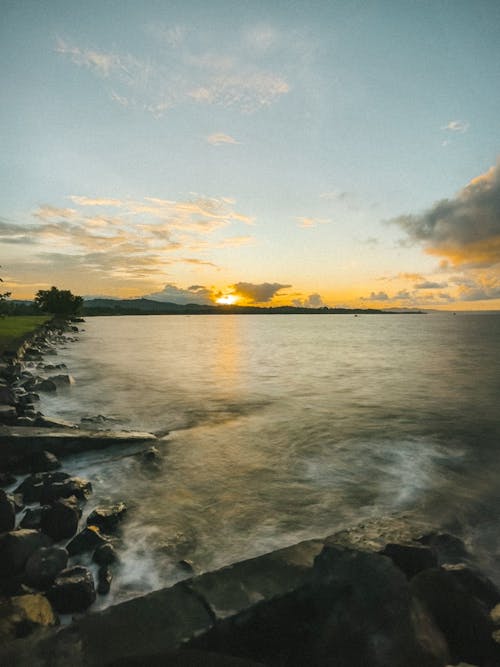 A Body of Water Under Blue Sky During Sunrise