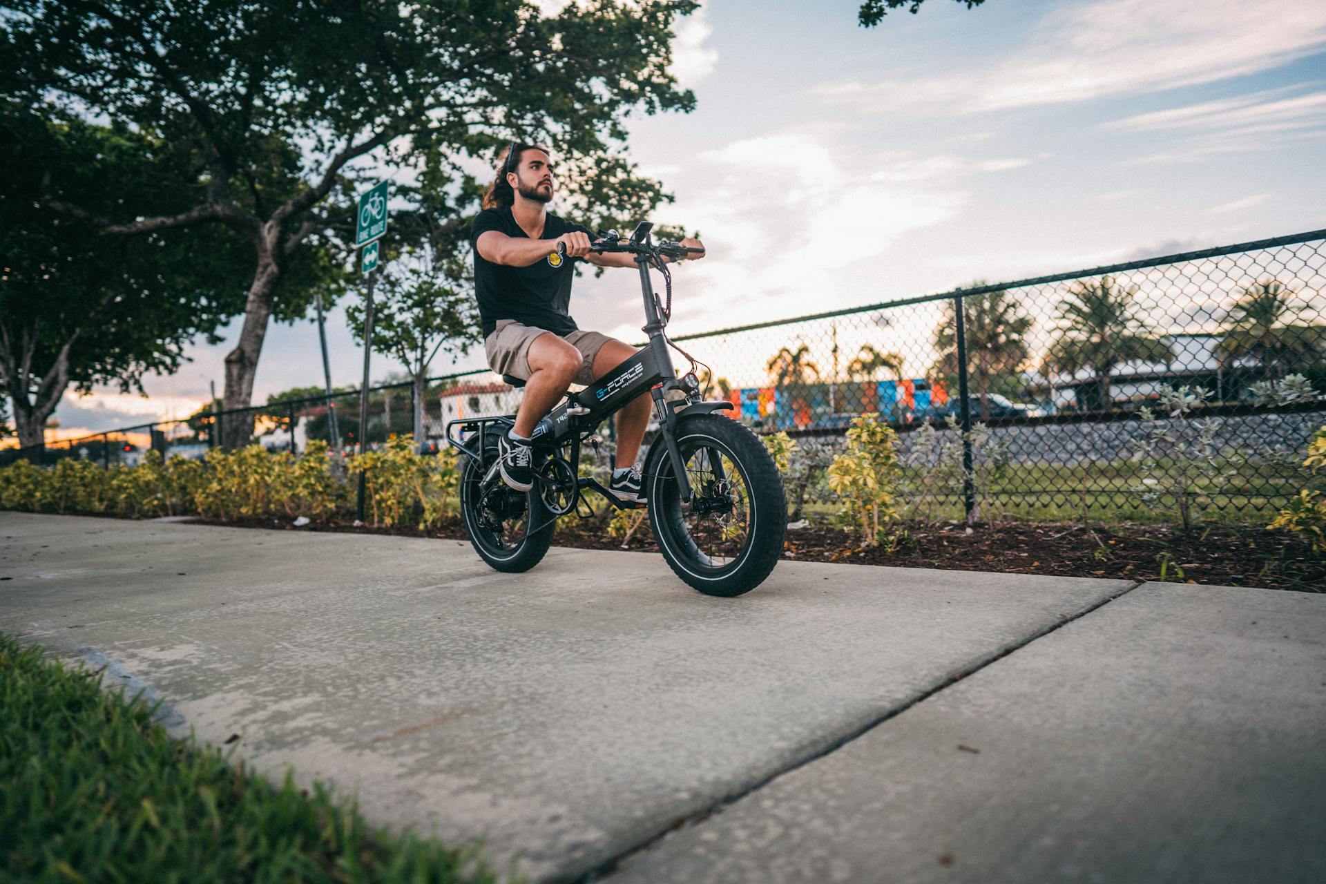 Young man on an electric bike cruising down a sunny outdoor pathway.
