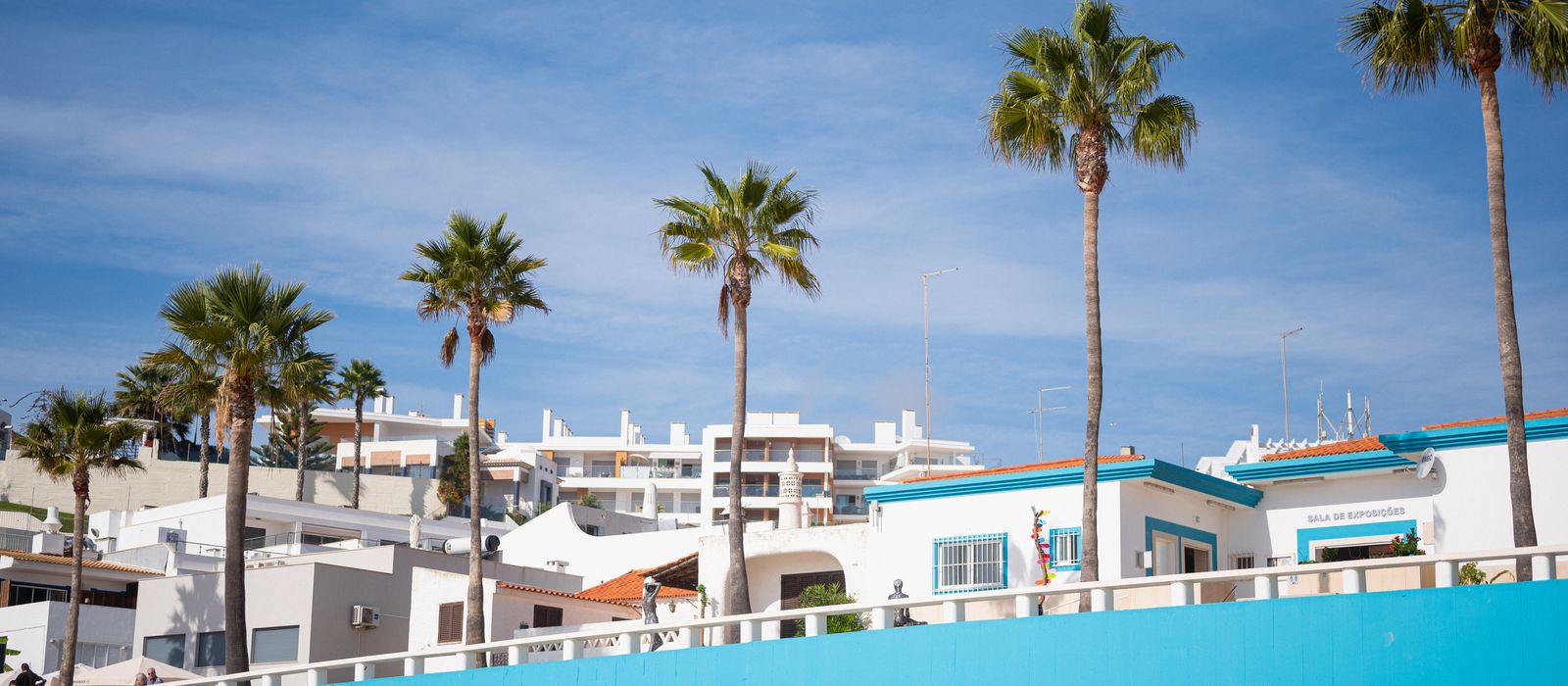 Bright Albufeira beachfront with charming houses and tall palm trees under a clear blue sky.