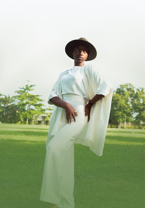 A Woman in White Clothes Standing on Green Grass Field with Her Hand on Her Waist