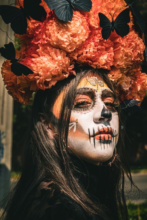 Free Artistic portrait of a woman in Dia de los Muertos makeup with a vibrant floral headpiece and butterfly adornments. Stock Photo