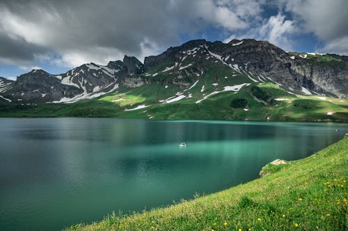 A Lake Near the Mountain with Green Grass Under the Cloudy Sky