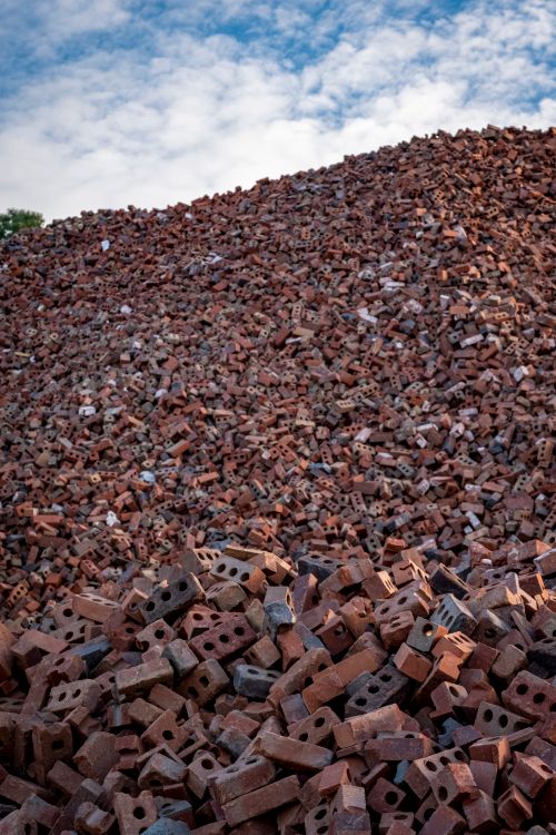Free A large heap of irregularly piled, used red bricks under a partly cloudy sky, showcasing construction waste. Stock Photo