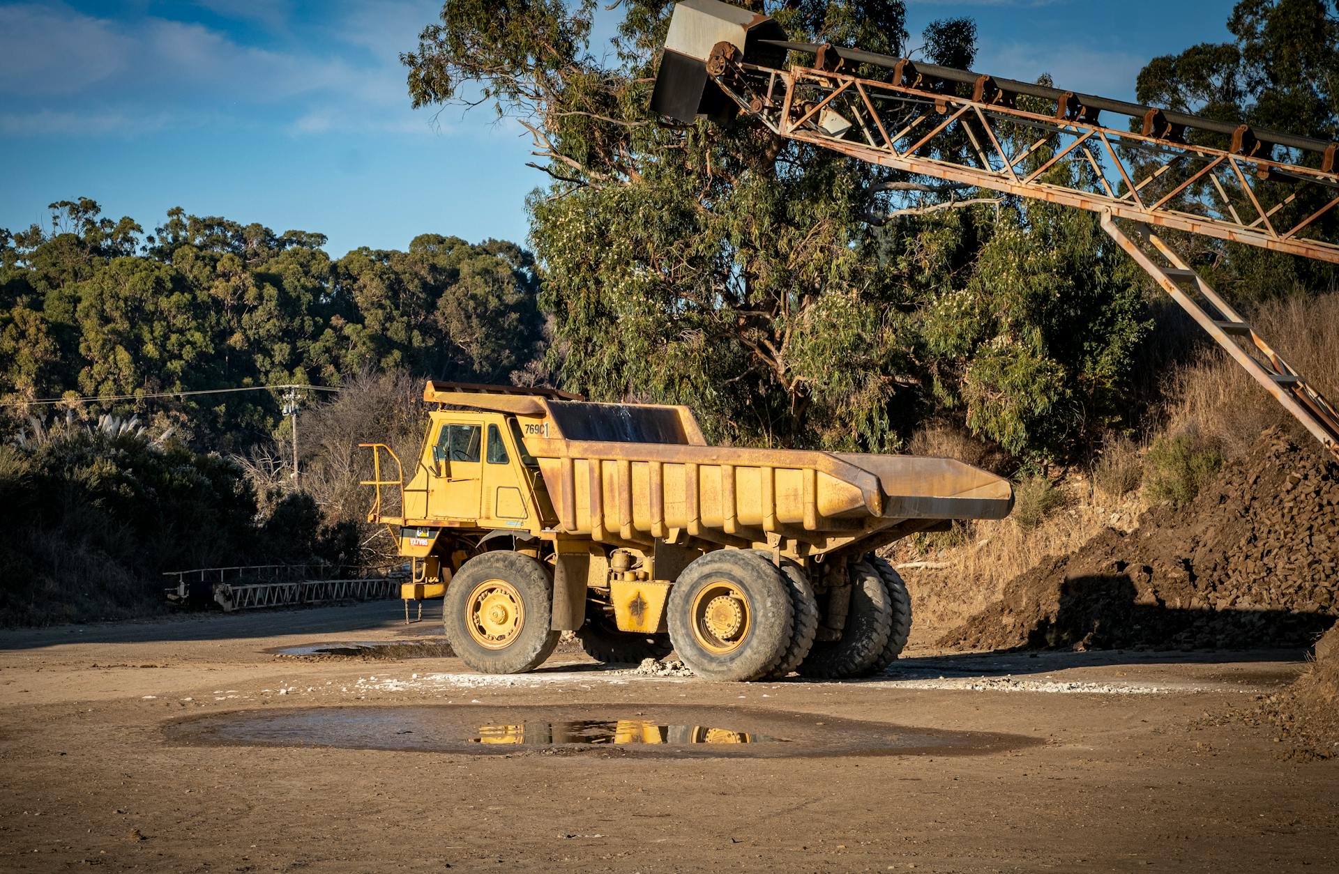 A large yellow dump truck parked at an outdoor construction site under a bright blue sky.