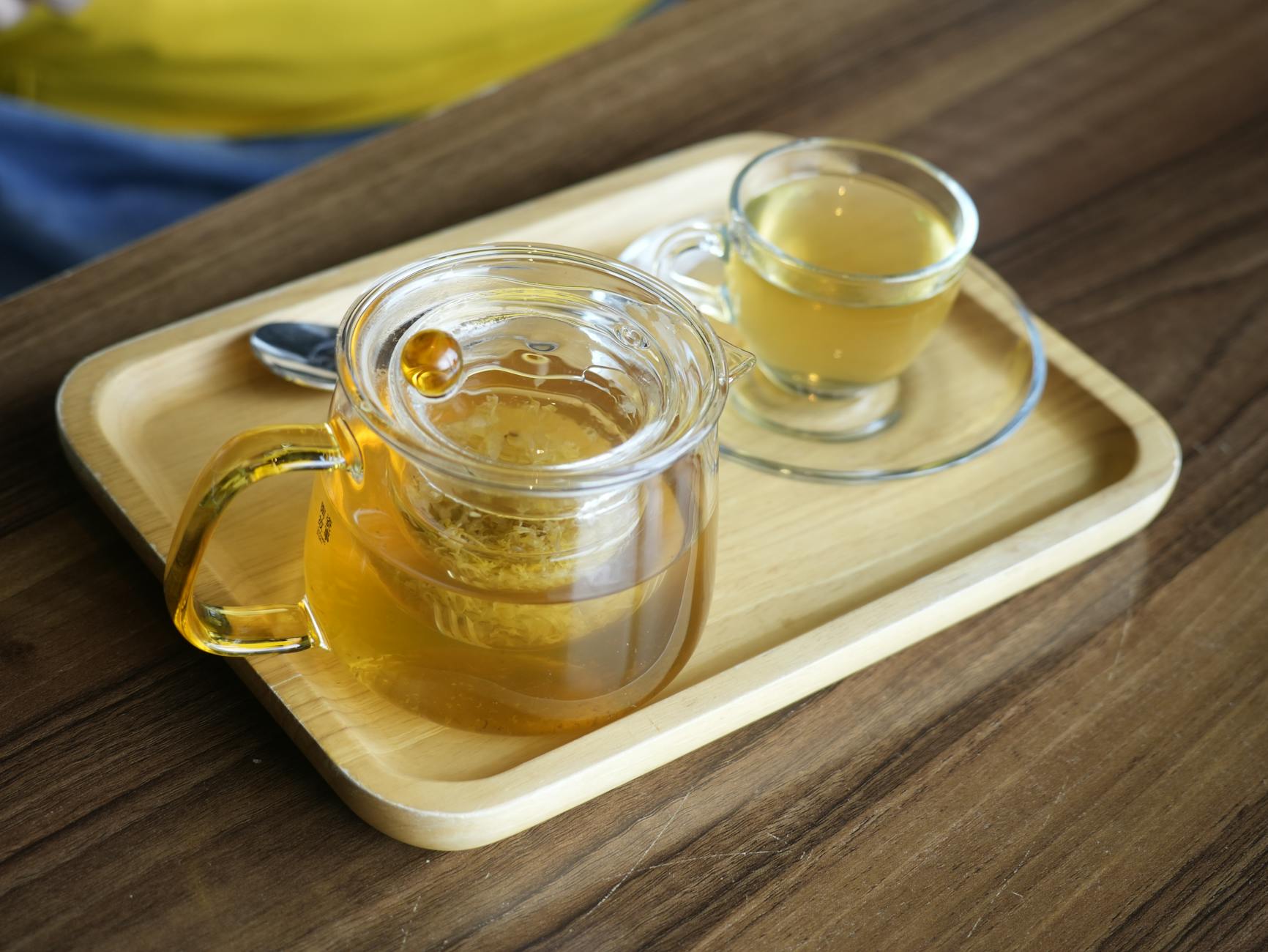 Honey In A Small Glass Jar With A Teaspoon Beside It, Placed On A Wooden Table Next To A Cup Of Herbal Tea