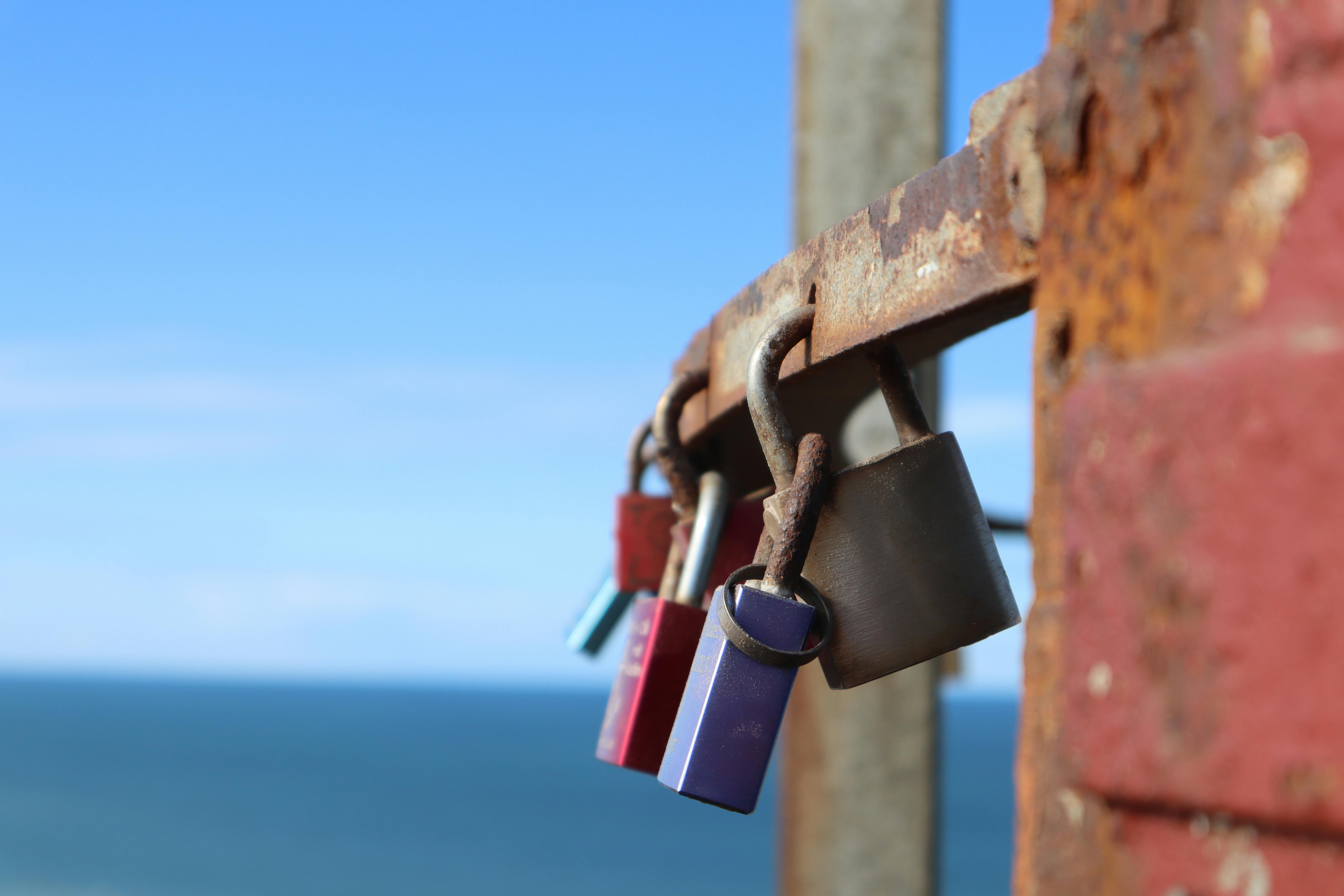 Close-up of vibrant padlocks on a rusty rail with the sea in the background, Rugbjerg, Danmark.