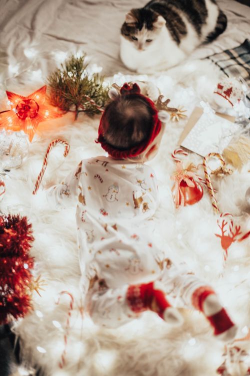 Free A cute baby in festive pajamas lies with a cat amidst Christmas decorations. Stock Photo
