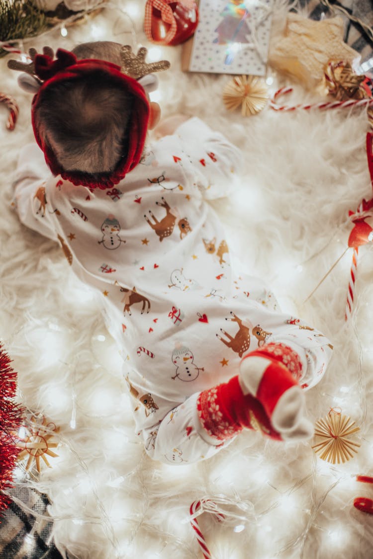 A Baby In A Christmas Romper Surrounded By Lights