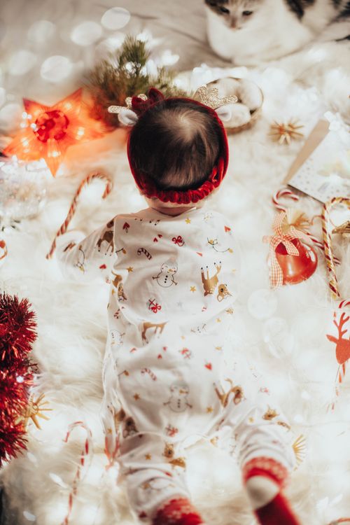 Free A baby in reindeer pajamas lying in a cozy Christmas setting with decorations. Stock Photo