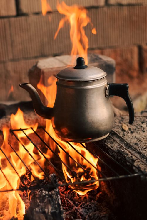 Free A classic metal kettle heats over an open flame on a grill, set outdoors for rustic cooking. Stock Photo