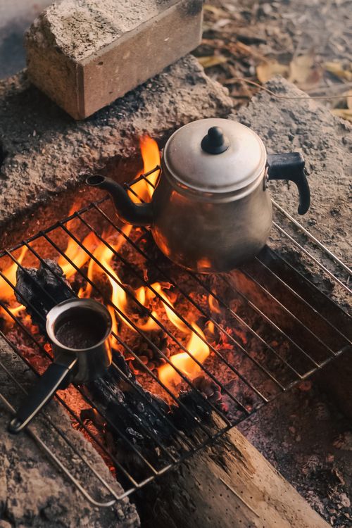 Free A kettle and pot heating over an open fire grill, creating a cozy campfire scene. Stock Photo