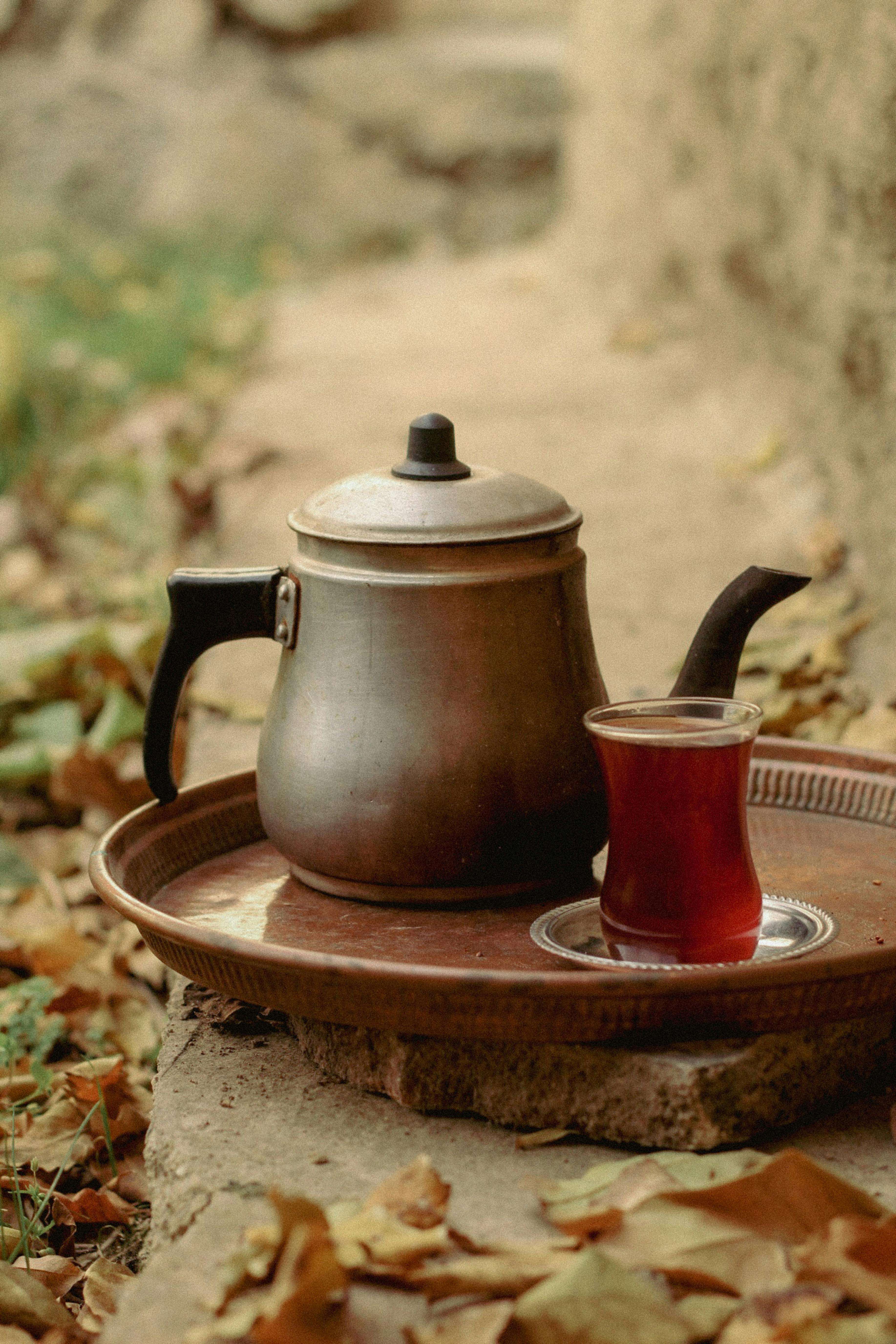 Cozy outdoor setting featuring a metal kettle and a glass of tea on a tray amidst autumn leaves.