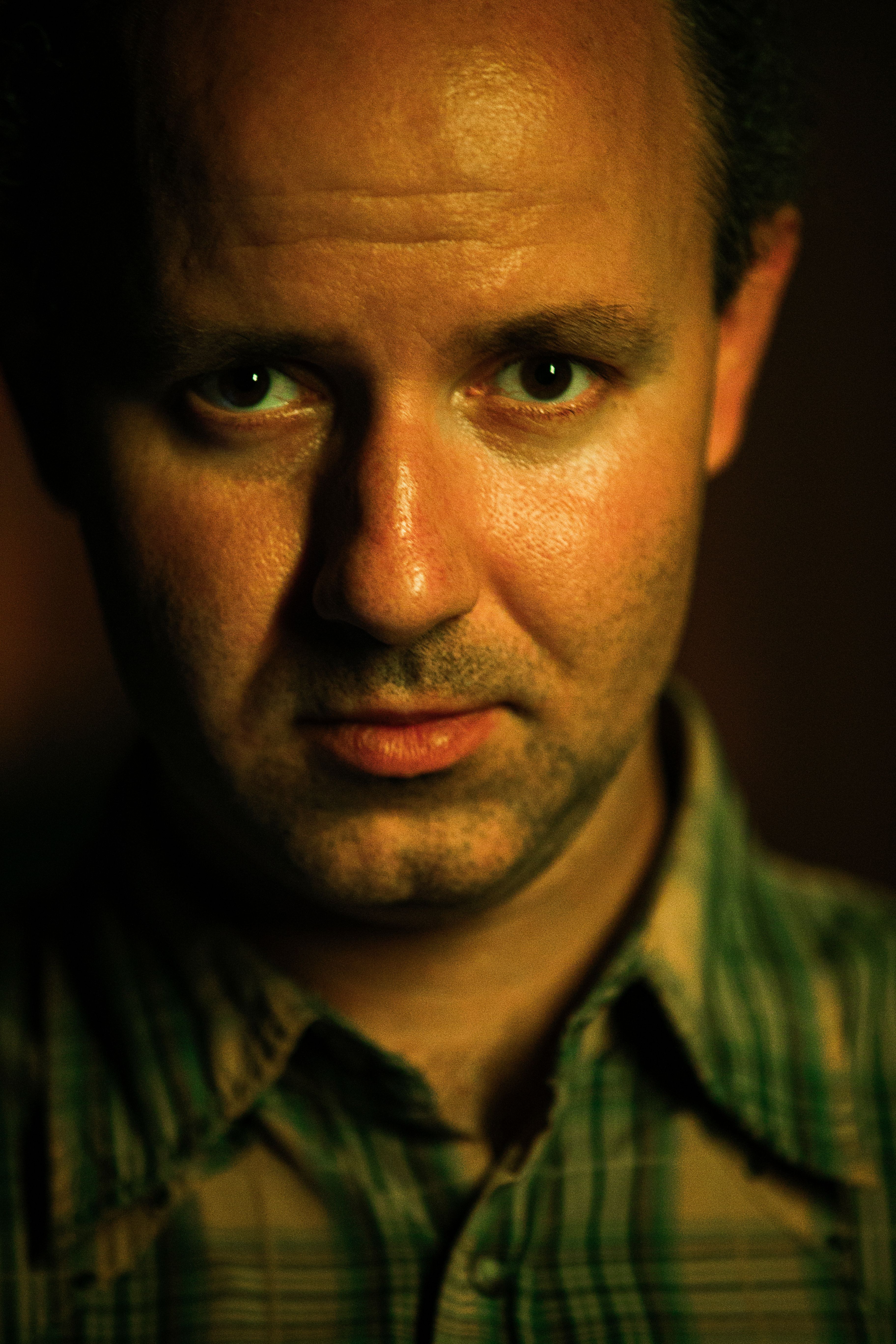 Close-up portrait of a man under warm lighting, capturing an intense gaze.