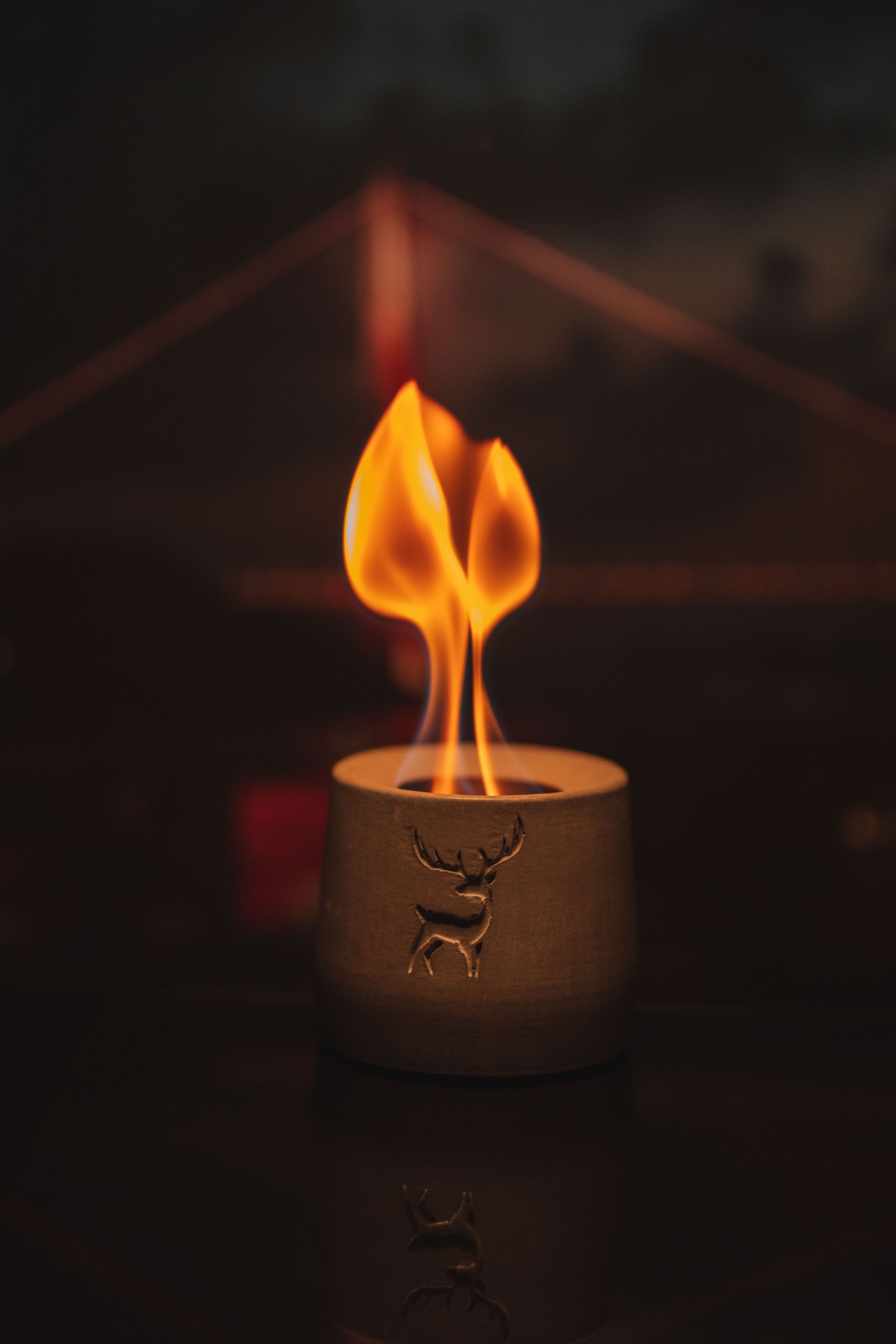 A candle with a deer motif burns warmly against a bridge silhouette, evoking a serene ambience.