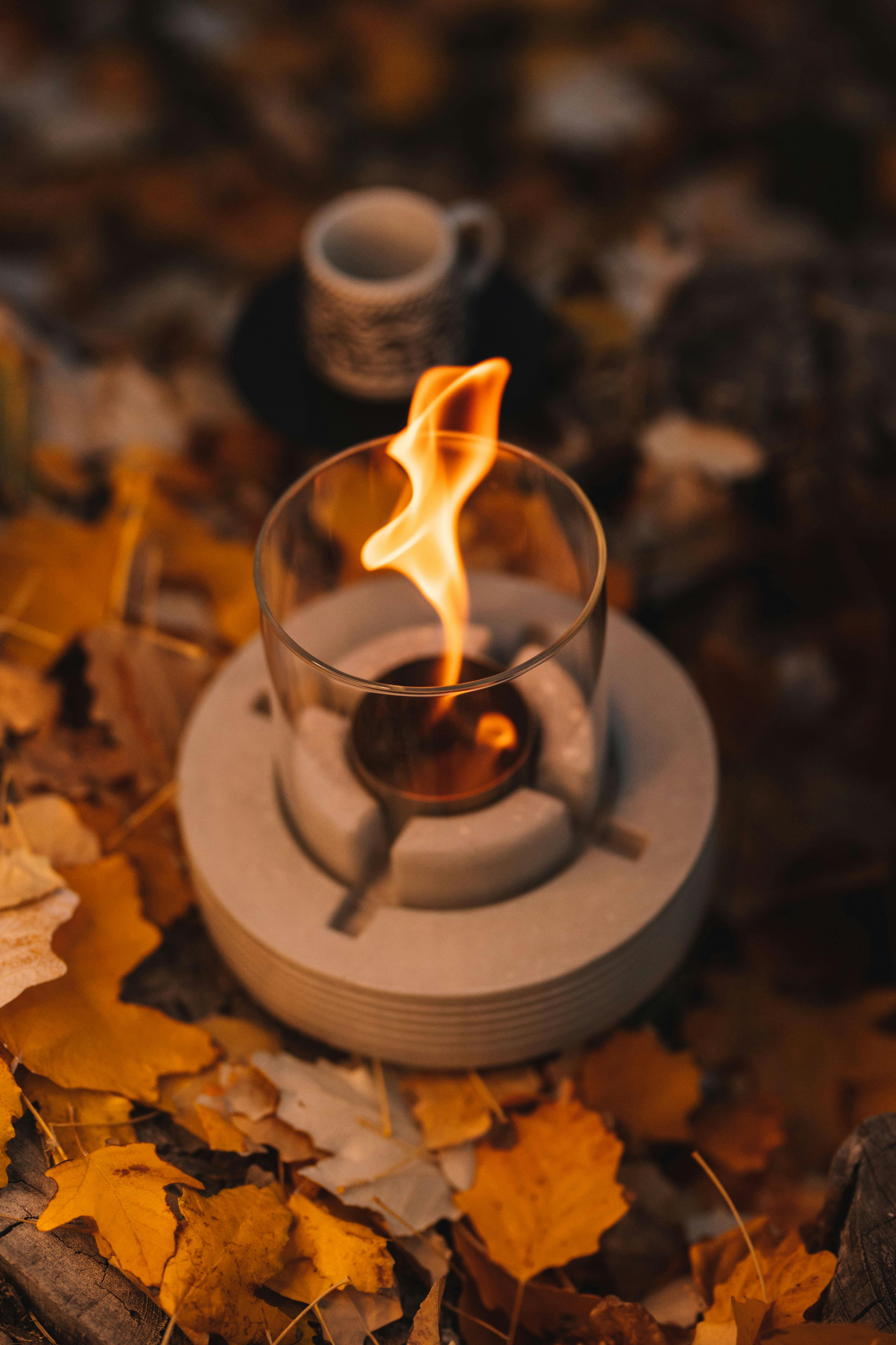 A warm autumn scene featuring candlelight with fallen leaves and a rustic coffee cup.
