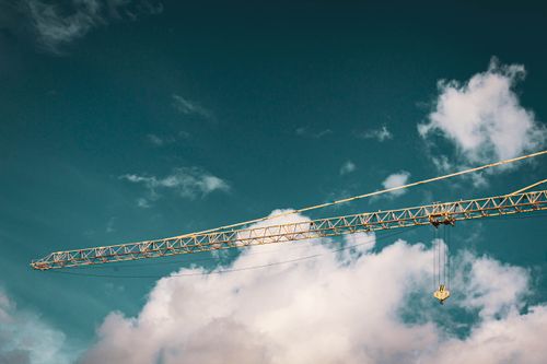 Free A tall tower crane set against a vibrant blue sky with fluffy clouds. Stock Photo