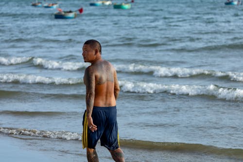 Shirtless Man with Body Tattoo Walking on Seashore