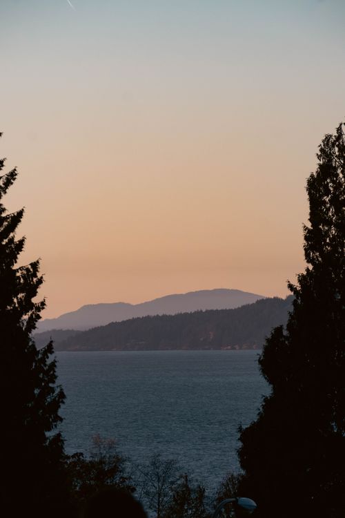 Free Serene sunset over Vancouver's mountains and lake, framed by trees, capturing the tranquil beauty of nature. Stock Photo