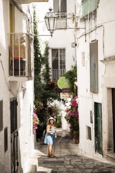 在意大利普利亚莱切的一条狭窄街道上，一名游客正漫步探索，街道两旁环绕着历史悠久的建筑和鲜艳的鲜花