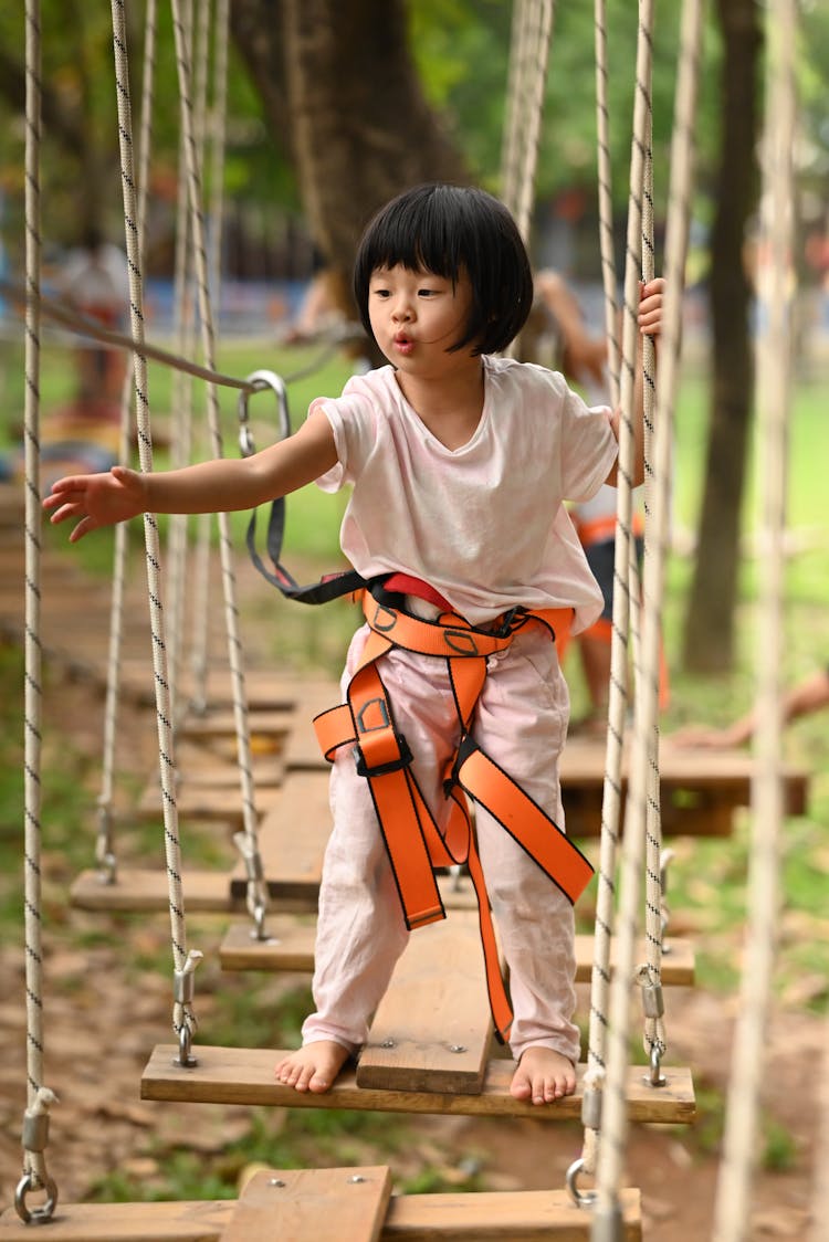 A Young Girl Wearing Harness While Stepping On A Wooden Panel