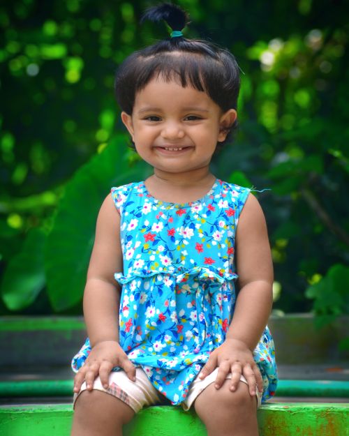 Free Cute toddler with a joyful smile sitting outdoors in a vibrant, colorful summer dress. Stock Photo