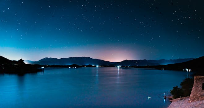 A serene night landscape featuring a starry sky over a calm lake with distant mountains. by JackerKun