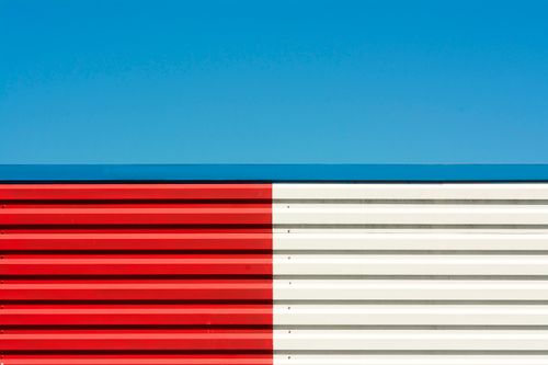 Free Stylish abstract image of a red and white striped wall with a vivid blue sky background, perfect for modern design projects. Stock Photo