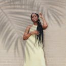 一位扎着辫子的时尚年轻女子自信地靠在阳光明媚的砖墙上摆姿势