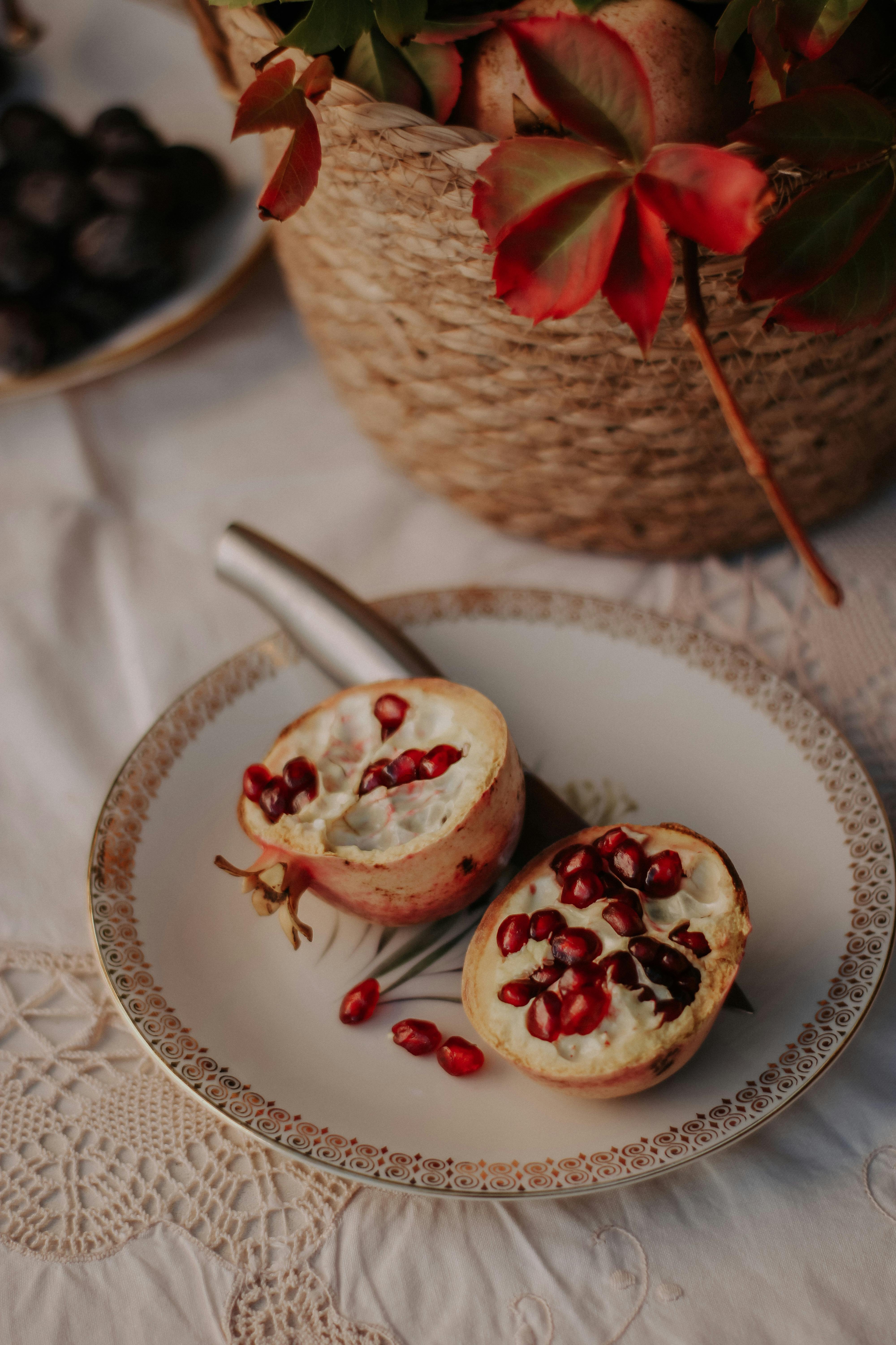 Juicy pomegranate halves displayed on a decorative plate with a rustic wicker basket in the background.
