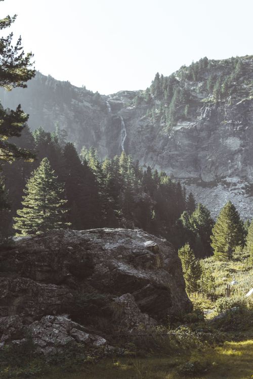 Free Peaceful mountain scene featuring lush forest, rocky formations, and a cascading waterfall. Stock Photo