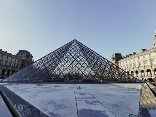 Free The iconic glass pyramid of the Louvre Museum stands strikingly against a clear blue sky. Stock Photo