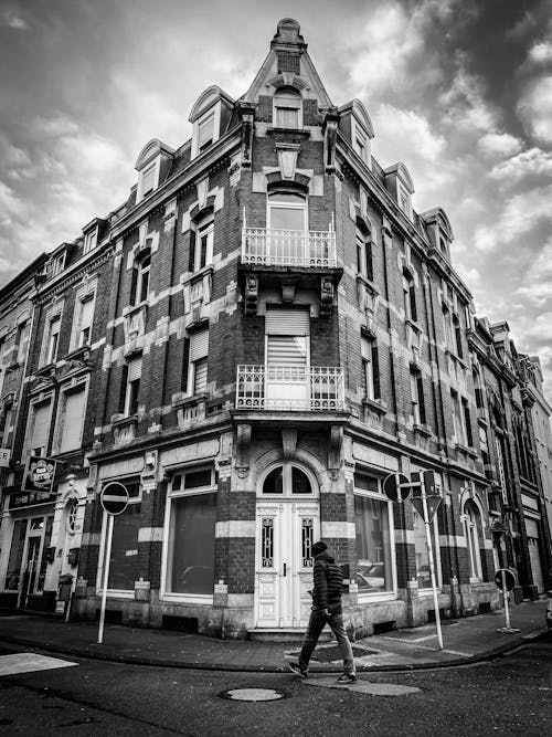 A Grayscale Photo of a Person Walking on the Street Near the Building