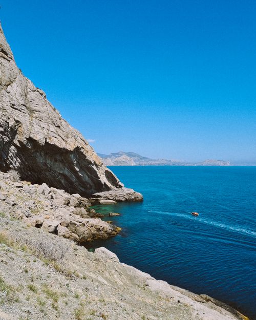 Free A majestic cliff overlooks a serene blue sea with clear skies and distant mountains. Stock Photo