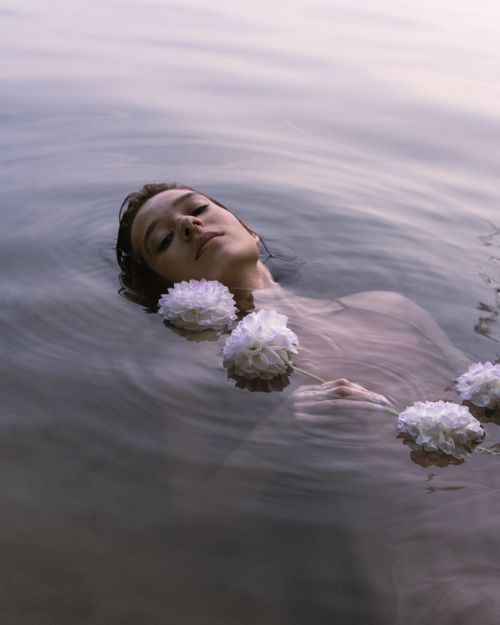 Free Tranquil image of a woman floating with flowers in calm water, embodying peace and elegance. Stock Photo