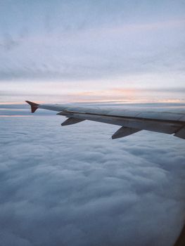 A stunning view of an airplane wing soaring above fluffy clouds during sunset, captured from a window seat.