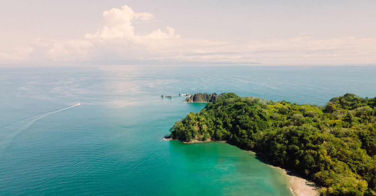Stunning aerial shot of a tropical island surrounded by clear blue sea and lush green landscape.