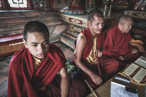 Free Three Tibetan monks in red robes meditate in a richly decorated monastery, focusing on spiritual practice. Stock Photo