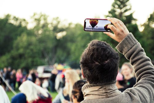 Free Man Holding Phone Capturing Hot Air Balloon Stock Photo