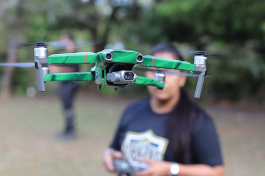 Close-up of a green drone in flight with a woman operator in a park setting.