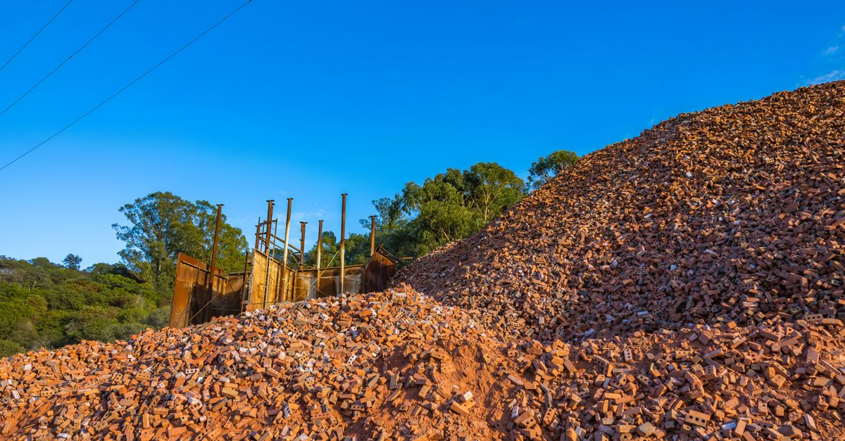 Photo by Robert So Large pile of red bricks at a construction site under clear blue sky.