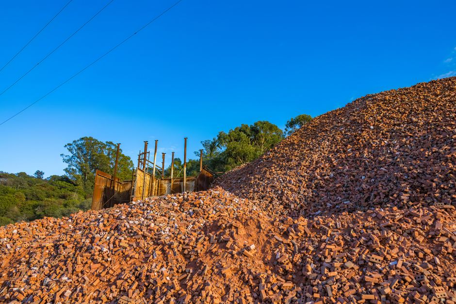 Photo by Robert So Large pile of red bricks at a construction site under clear blue sky.