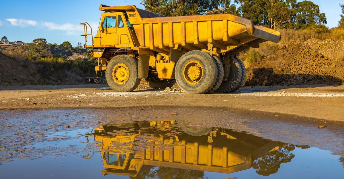 Yellow dump truck with reflection in water at a mining site, exhibiting industry machinery.